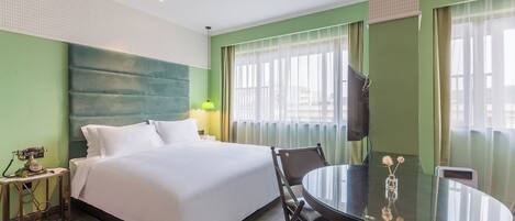 A hotel room with a bed, a round table, a chair, a TV, and a small table with a lamp and decorative items.