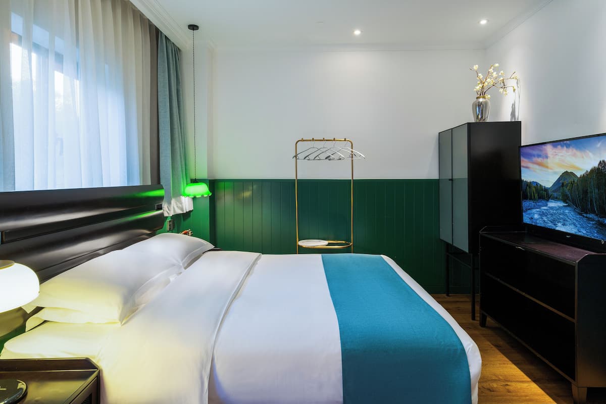 Una habitación de hotel con una cama, un televisor, un jarrón con flores y una pared verde.