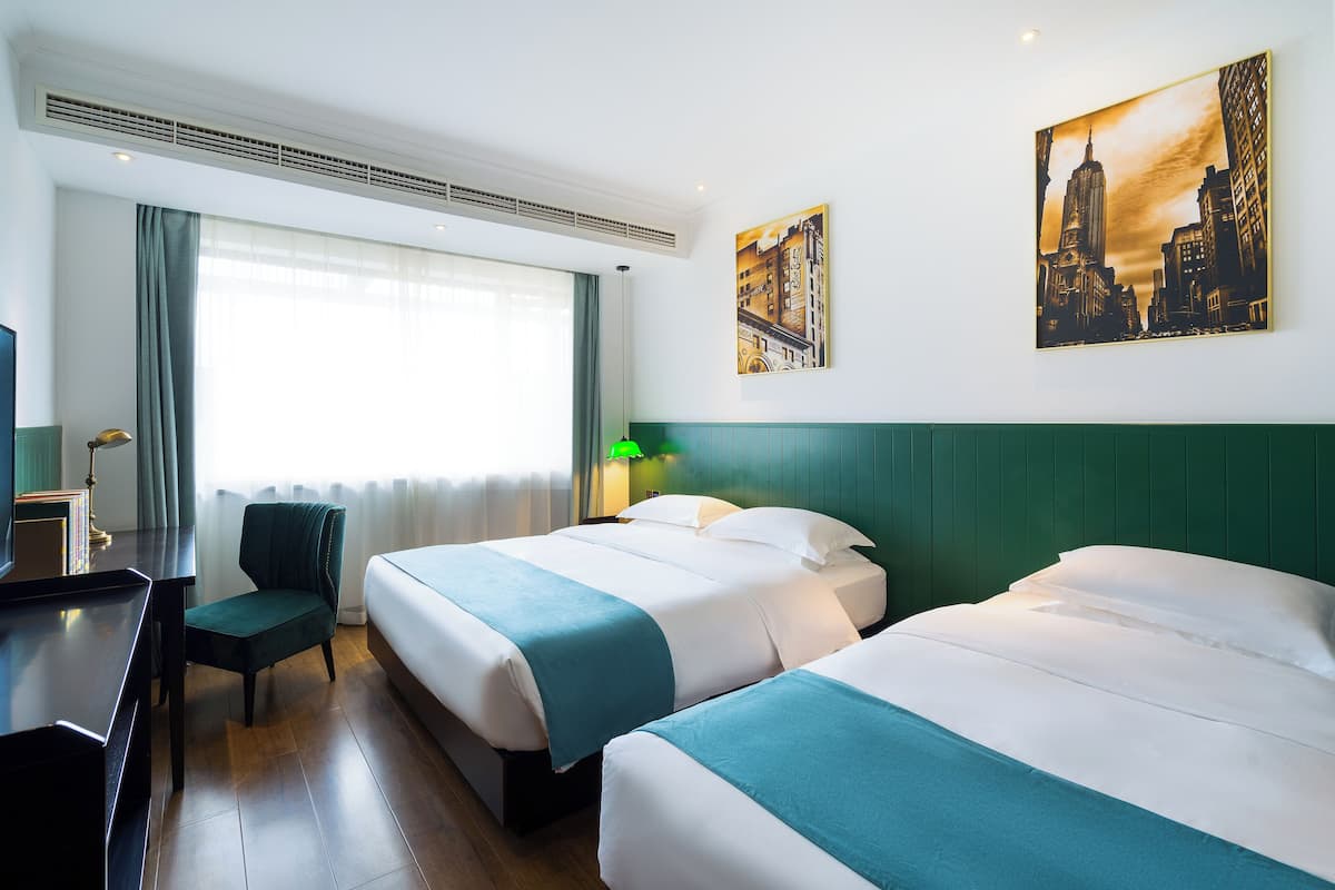 Habitación de hotel con dos camas, un escritorio, una silla y un ventanal grande.
