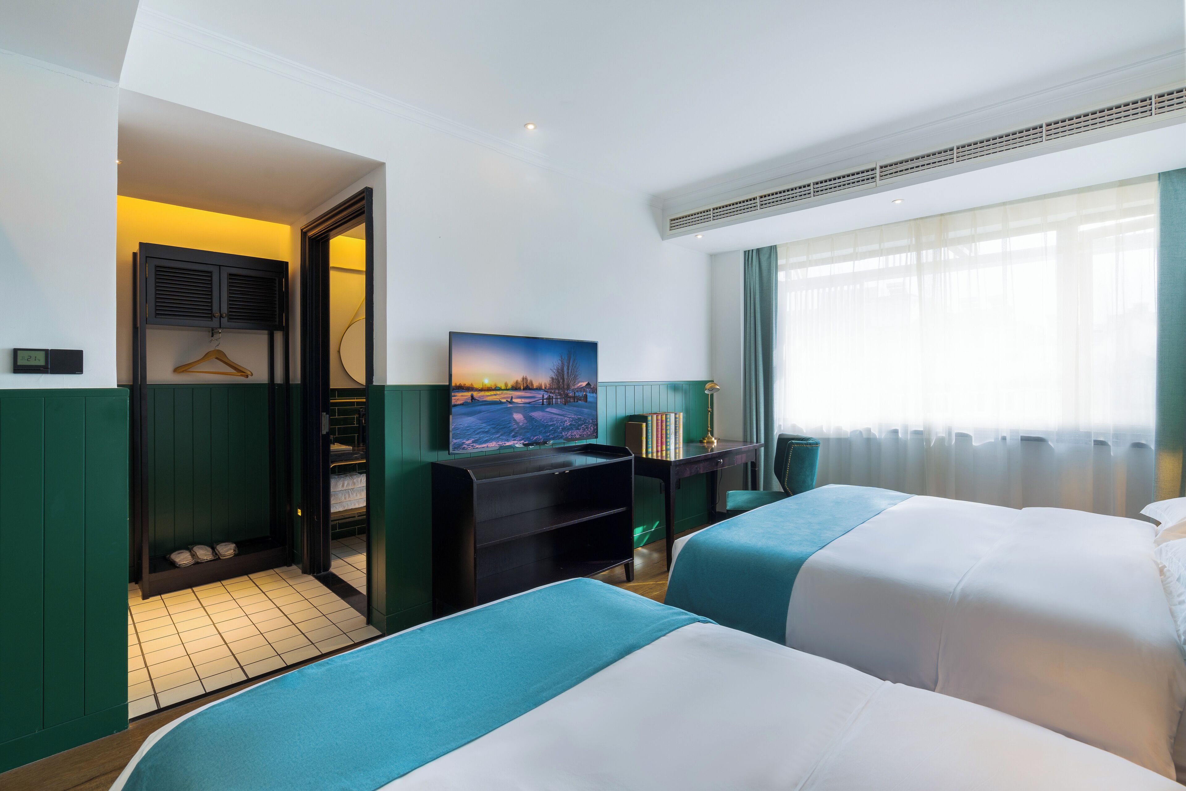 A hotel room with two beds, a desk, a TV, and a painting.