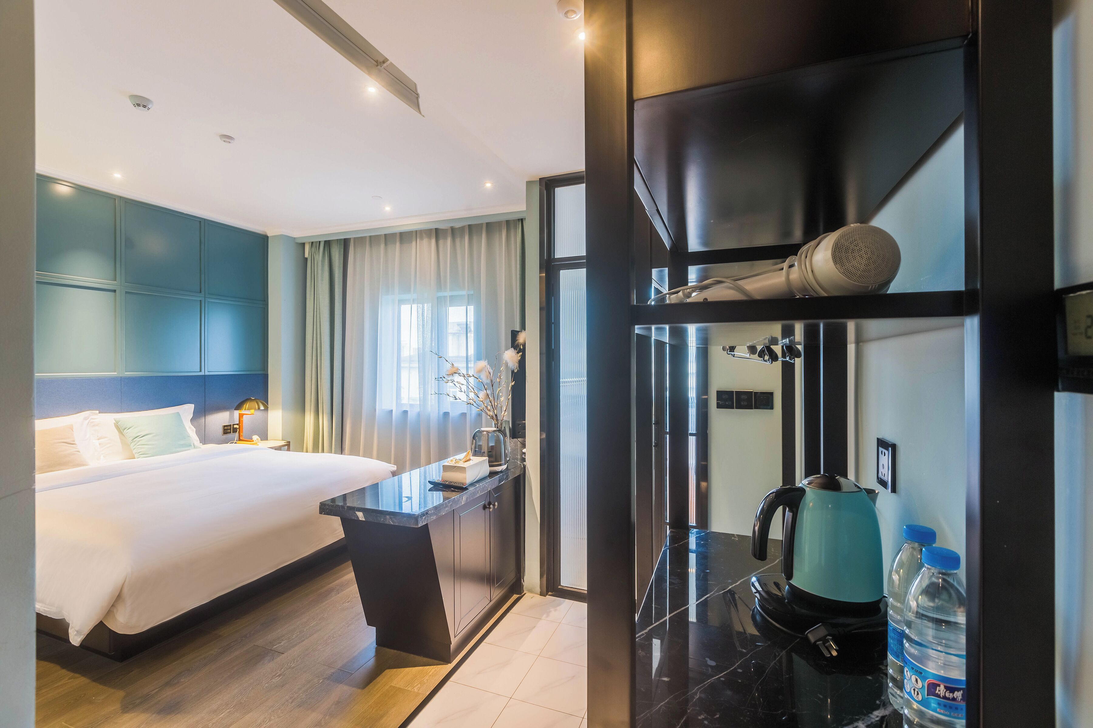 Ein modernes Hotelzimmer mit einem großen Bett, einem Schreibtisch mit Wasserkocher und einem Wasserspender.