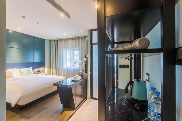 A modern hotel room with a large bed, a desk with a kettle, and a water dispenser.