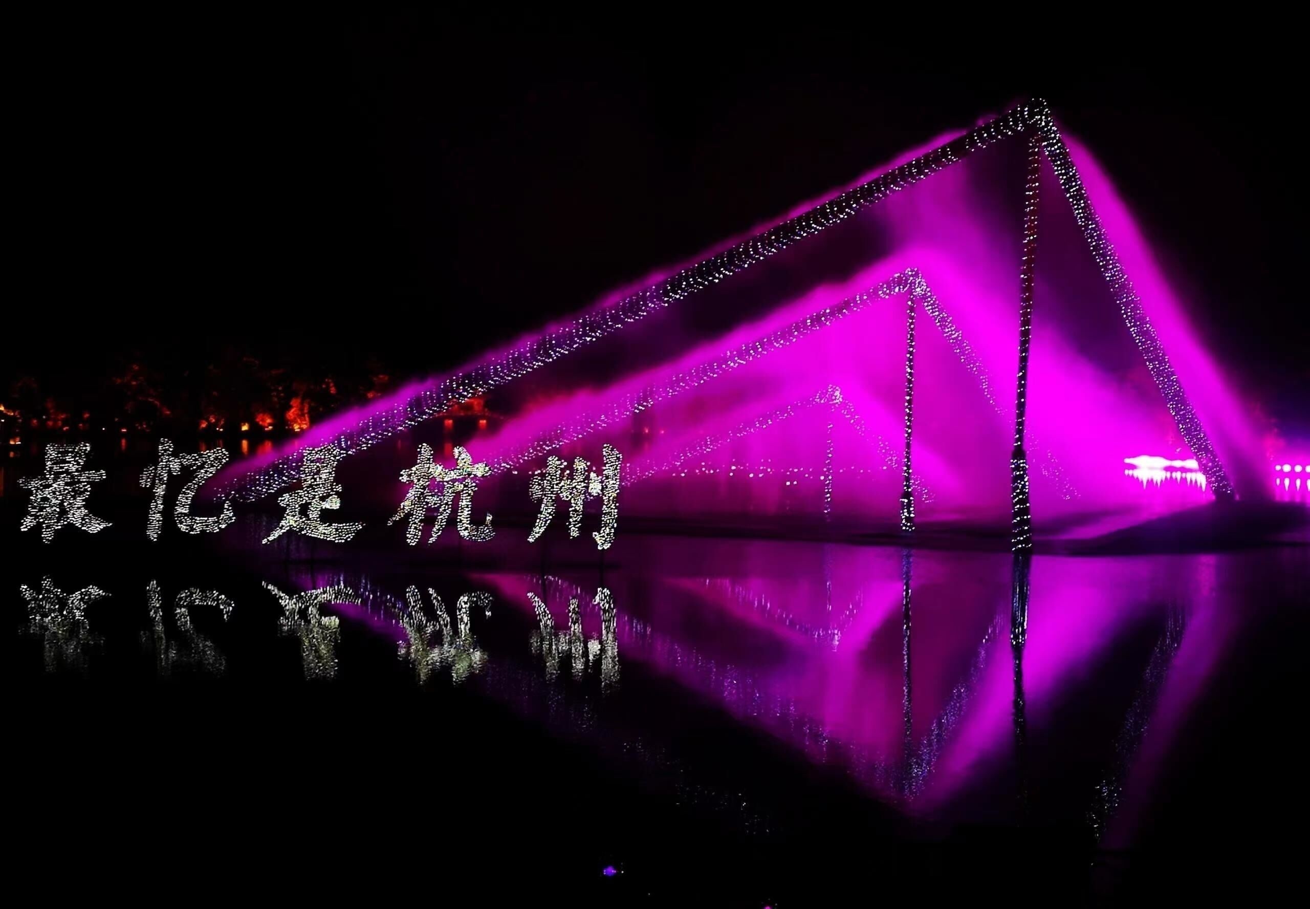A nighttime view of a bridge illuminated with purple lights, reflecting on the water below.