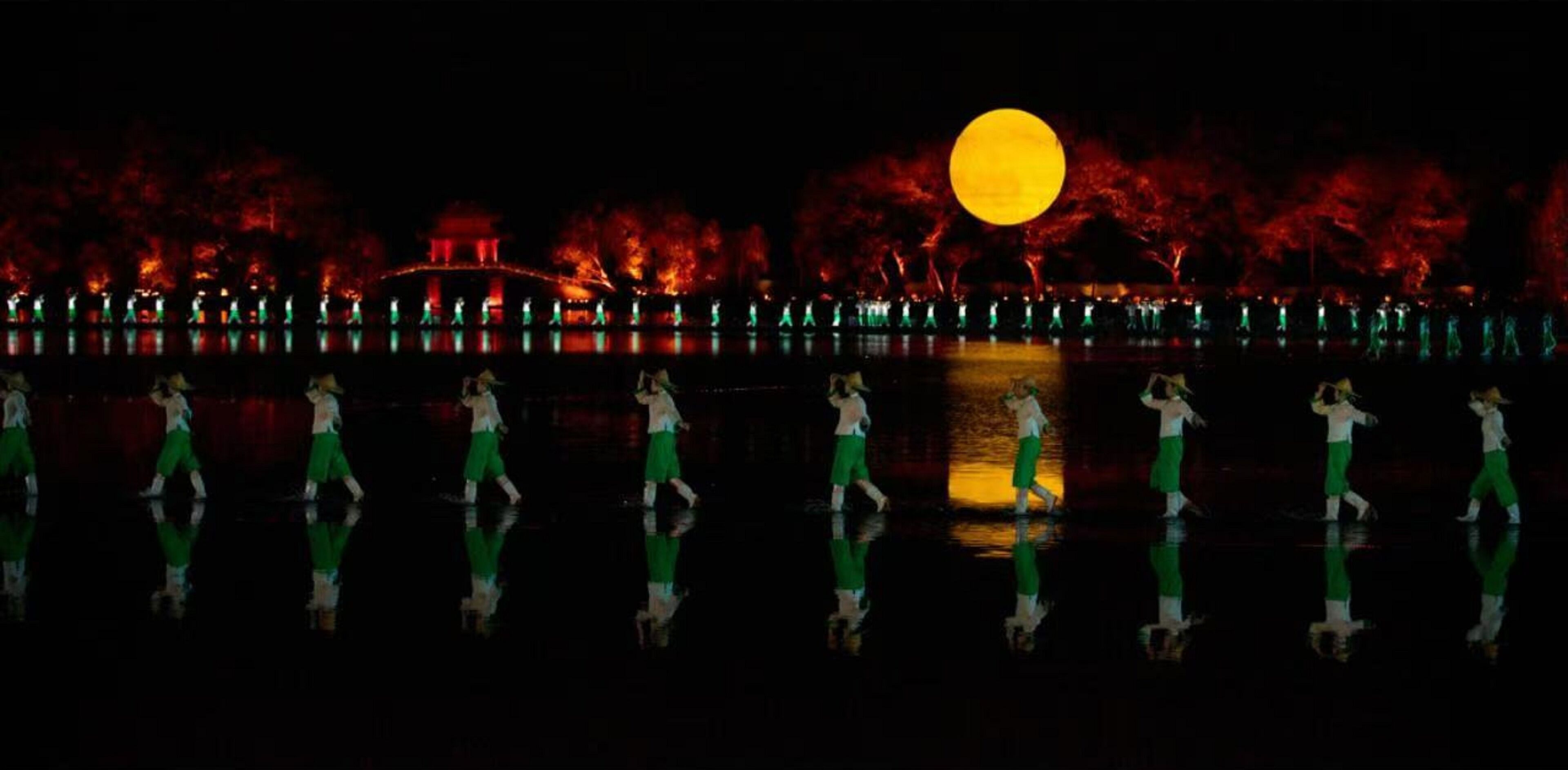 A nighttime scene with a full moon, illuminated trees, and a reflective water surface.