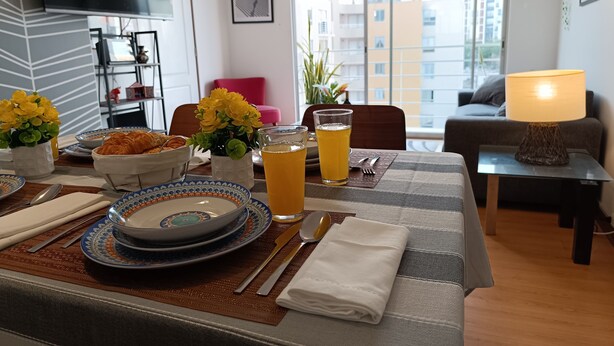 A dining area with a table set for breakfast, including plates, cutlery, and a glass of orange juice.