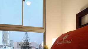 A hotel room with a bed, a window with a view of the city, and a red pillow with the hotel's name.