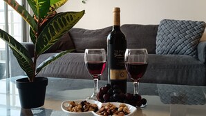 A living room with a glass coffee table, a potted plant, a bottle of wine, two wine glasses, and a bowl of nuts.