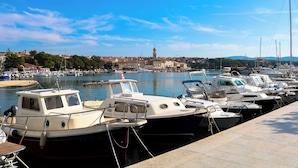 A marina with several boats docked, a clear sky, and a distant view of a town with a prominent tower. - Studio near the Old Town (Krk)