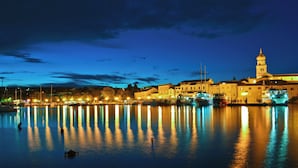 A waterfront cityscape at night with illuminated buildings reflecting on calm water. - Studio near the Old Town (Krk)