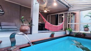Área de piscina com rede, plantas em vasos e espaço para sentar.
