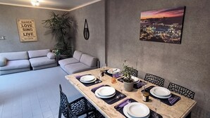 Uma área de refeições com uma mesa posta para quatro pessoas, um sofá e uma pintura da paisagem urbana na parede.