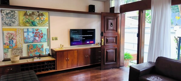 Un salón con televisor, armarios de madera, obras de arte en la pared y una puerta que da al exterior.
