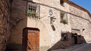 Un edificio de piedra con una puerta de madera grande, una ventana pequeña con una reja de metal y un cartel con un escudo.