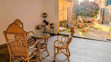 A wicker chair and table set in a room with a view of a courtyard.