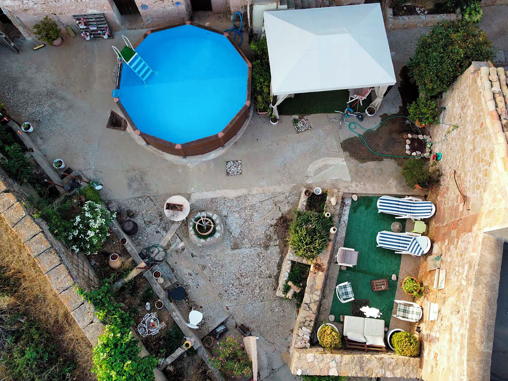 Une piscine extérieure, un espace de détente couvert et un petit jardin agrémenté de sièges et de plantes.