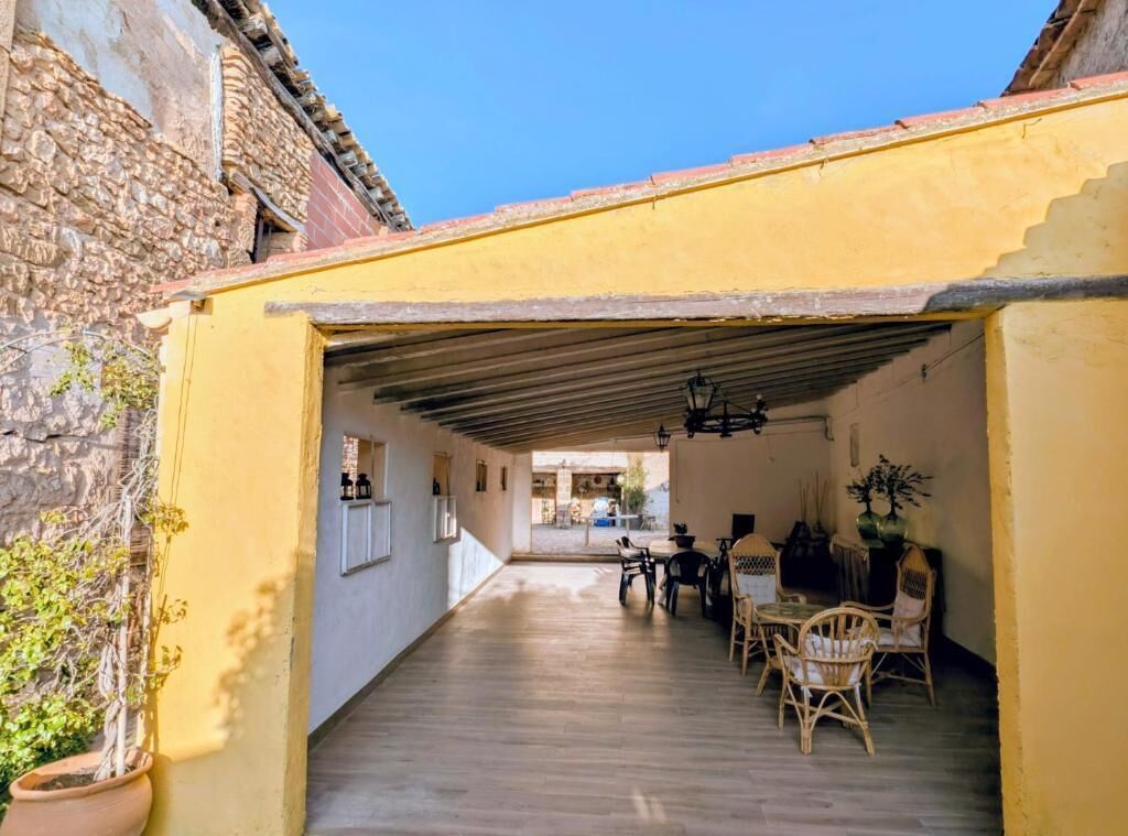 Un espace extérieur abrité doté d’un plancher en bois, de murs jaunes et d’un bâtiment en pierre en arrière-plan.