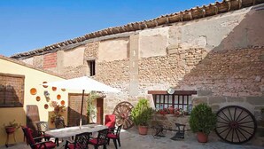 Un patio exterior con mesa y sillas, muros de piedra y plantas en macetas.