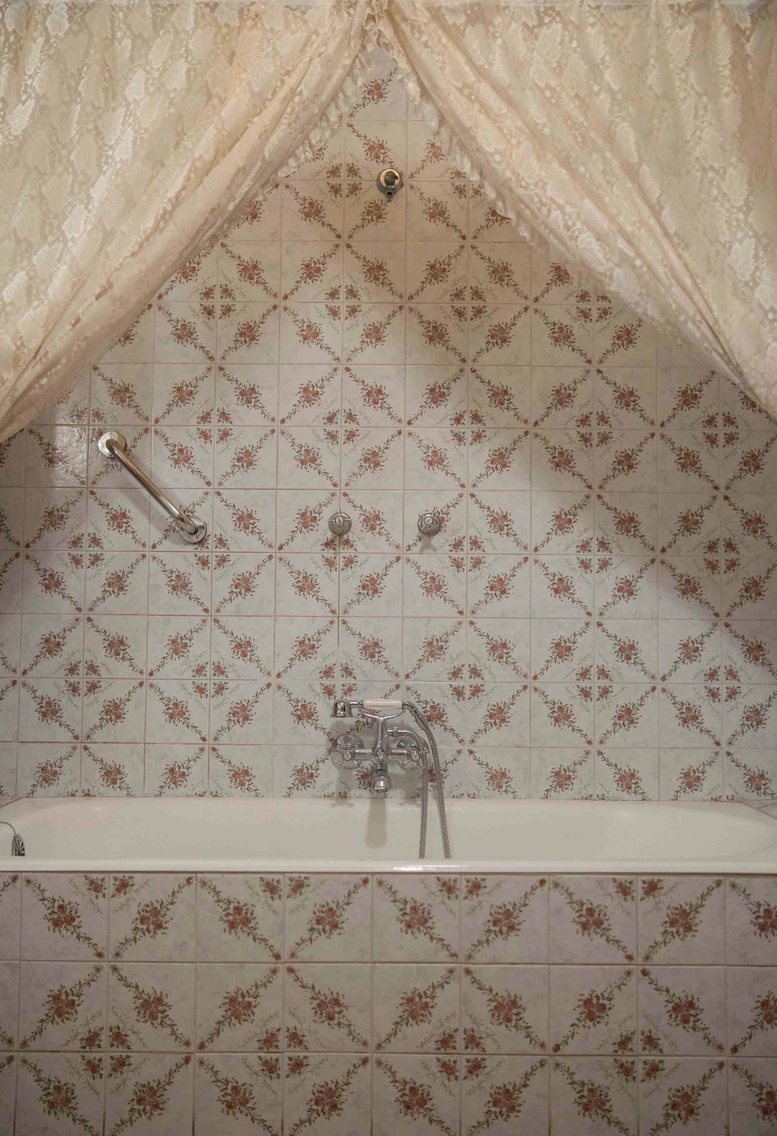 Een badkamer met een badkuip, betegeling met bloemenmotieven en een handdoekhouder.