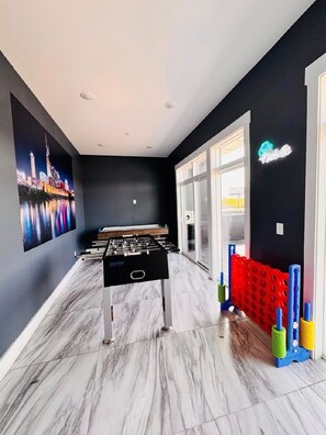 A room with a foosball table, a cityscape painting, and a neon sign.