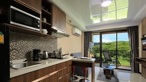 A modern kitchen with a Sharp microwave, a tiled backsplash, a sink, and a dining area with a view of greenery. - Naiharn Condominium 1 bedroom 36 sq. m. (Rawai)