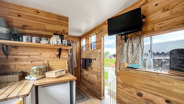 Een houten interieur met een keuken, een aan de muur bevestigde televisie en een raam met uitzicht op de omgeving.