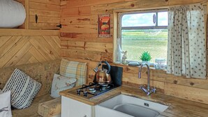 Een rustiek houten interieur met een keukenhoek, een fornuis en een spoelbak, een raam met gordijnen, en een poster aan de muur.