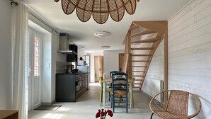 Una sala moderna con una mesa de comedor de madera, una silla de mimbre y una lámpara de techo original. Se ve una escalera al fondo que conduce a otro nivel.
