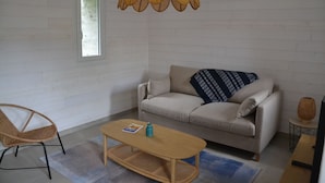 Una sala de estar con un sofá, una mesa de centro de madera, una silla de mimbre, una lámpara colgante y una pequeña mesita auxiliar.