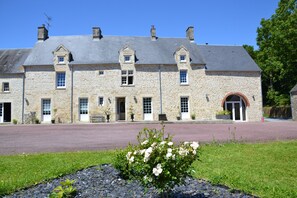 A stone building with a symmetrical facade, multiple windows, and a central entrance with a red arch. - A quiet, welcoming house for 4 people, 15 minutes from Utah Beach (Picauville)