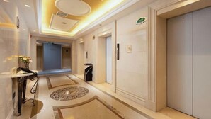 En hotelgang med marmorgulv, et rundt dekorativt gulvtæppe, en reception og en lukket elevator.