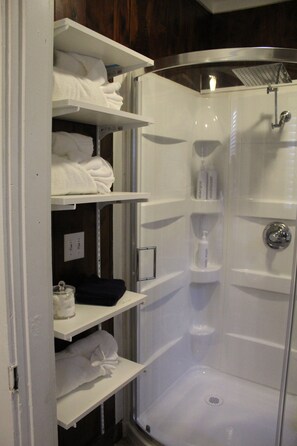 A walk-in shower with a glass door, white shelves with towels, and toiletries.