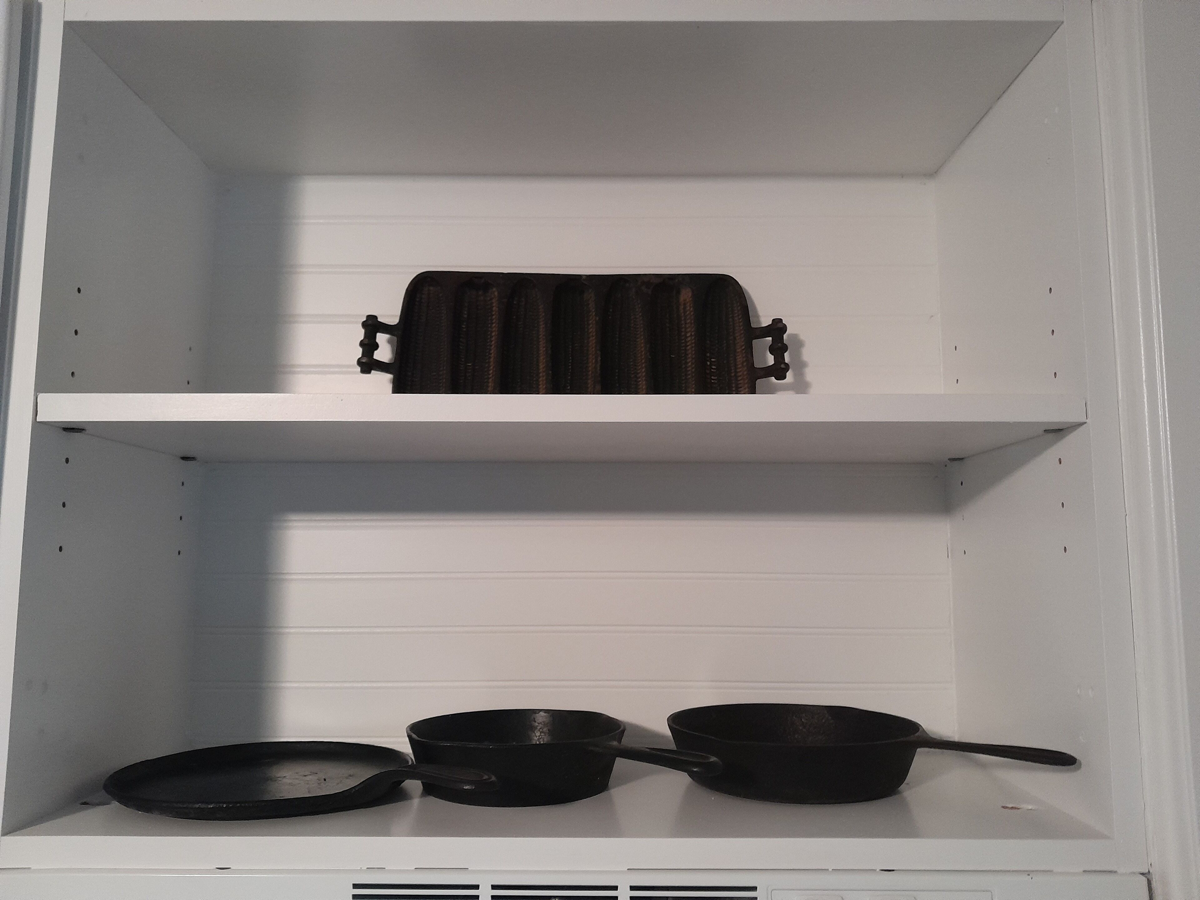 A kitchen with white cabinets and a black pan on the lower shelf.
