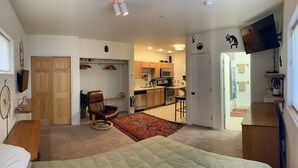 Een compact studio-appartement met een bed, een stoel, een keukenhoek en een televisie.