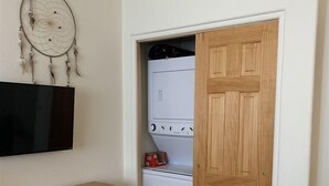 Een kleine kamer met een houten deur, een witte wasmachine en een wandgemonteerde televisie.