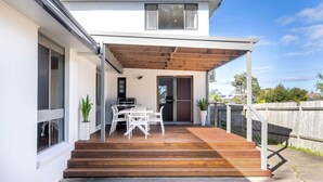 Une maison moderne dotée d’un patio couvert, d’un coin repas avec des meubles blancs et d’une grande fenêtre.