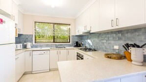 Une cuisine moderne avec des meubles blancs, un lave-vaisselle, une cuisinière à gaz et une fenêtre donnant sur un espace verdoyant.