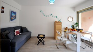Una sala de estar moderna con un sofá, una mesa de comedor con sillas, una mesita auxiliar y un adorno en la pared.