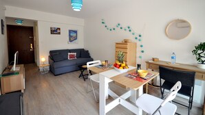 Una sala moderna con un sofá, una mesa de comedor y sillas. Hay una pequeña mesita de noche con una lámpara, un aparador de madera y un espejo en la pared.