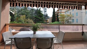Un balcón con una mesa y sillas, una planta en maceta y vistas a edificios y árboles.