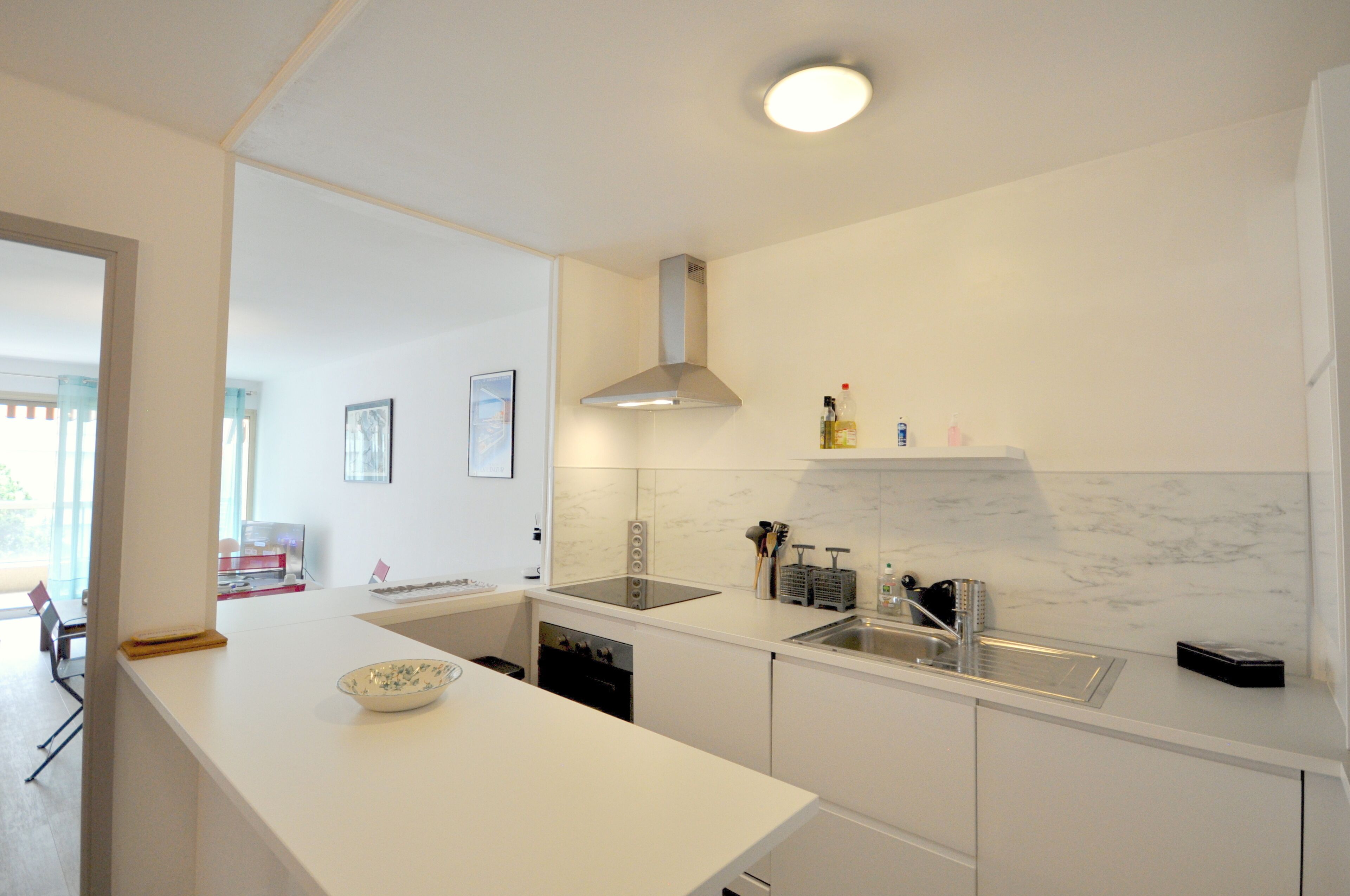 Une cuisine moderne avec des meubles blancs, une hotte en acier inoxydable et un pare-feu en marbre.