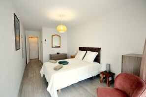 A bedroom with a bed, bedside tables, a mirror, a hanging light fixture, and a chair.