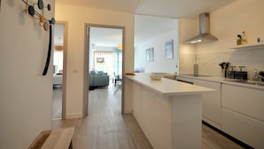 Cocina moderna con armarios blancos, una isla central y estufa integrada. Se ve un área de comedor al fondo.