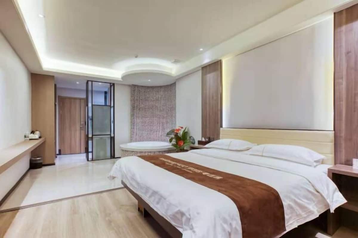 Una camera d'albergo moderna con un letto grande, un piccolo tavolino rotondo e un bagno con parete divisoria in vetro.
