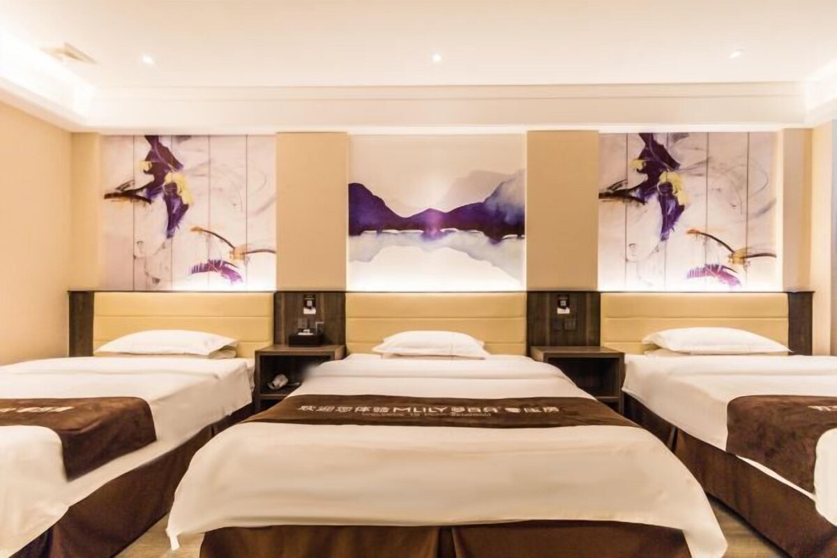 Ein Hotelzimmer mit drei Betten, einem großen abstrakten Gemälde an der Wand und einer Minibar.