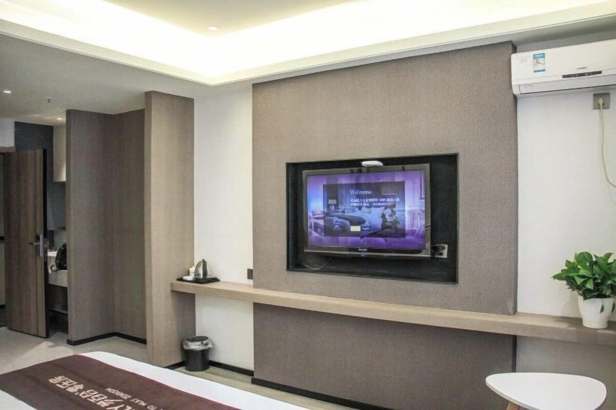 Ein modernes Hotelzimmer mit einem an der Wand montierten Flachbildfernseher, einer kleinen Ablage darunter und einer Zimmerpflanze zur Rechten.