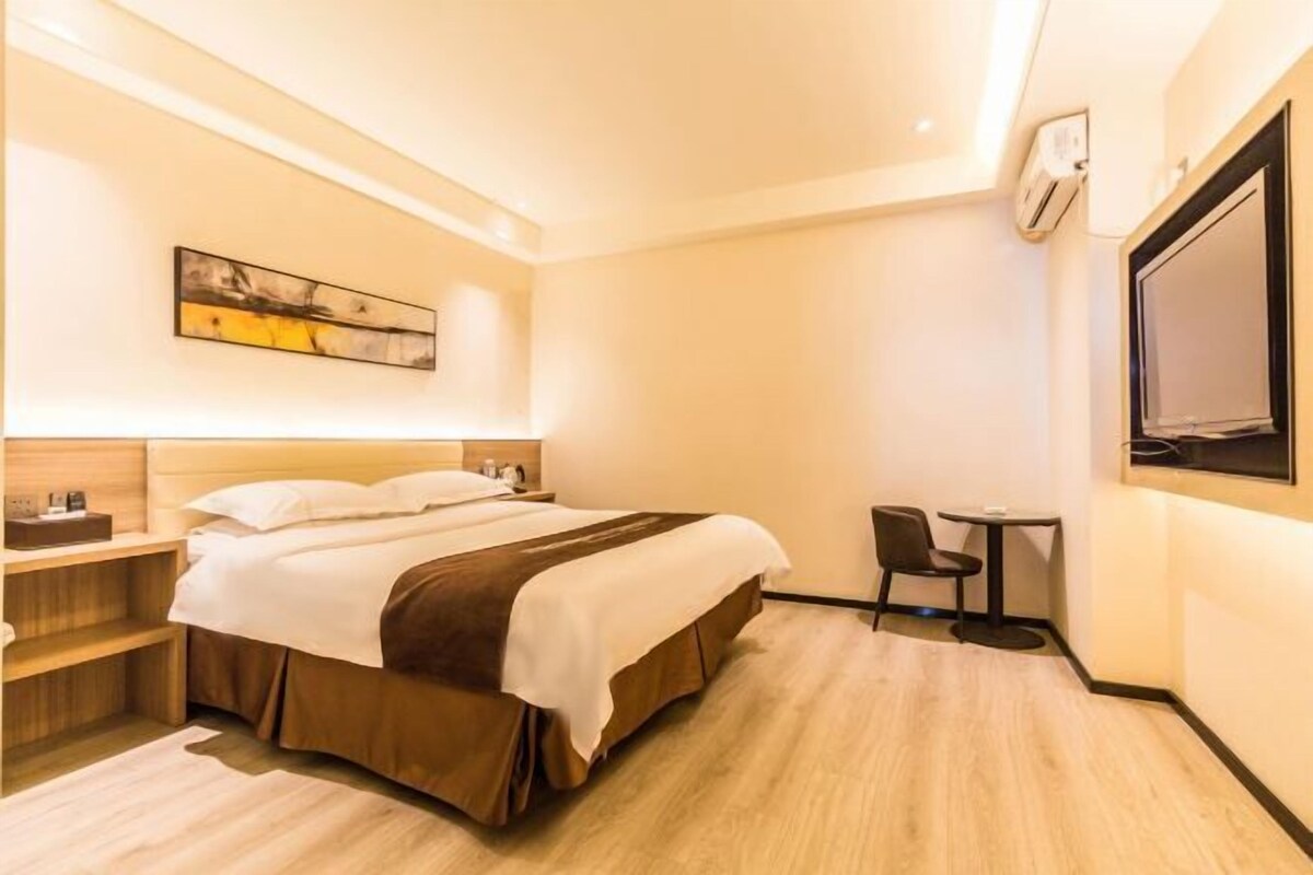 Ein Hotelzimmer mit einem Bett, Nachttischen, einem kleinen Schreibtisch, einem Sessel, einem Fernseher und einem Bild an der Wand.