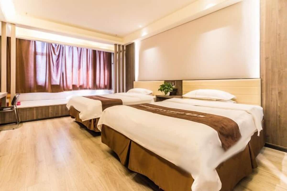 Camera d'albergo con due letti, pavimento in legno, un'ampia finestra con tende e una palette colori neutra.