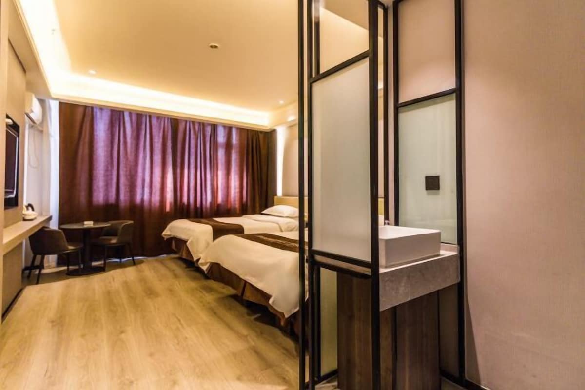 Ein Hotelzimmer mit Holzboden, zwei Betten, einem Schreibtisch mit Stühlen, einem großen Fenster mit Vorhängen und einem Spiegel.