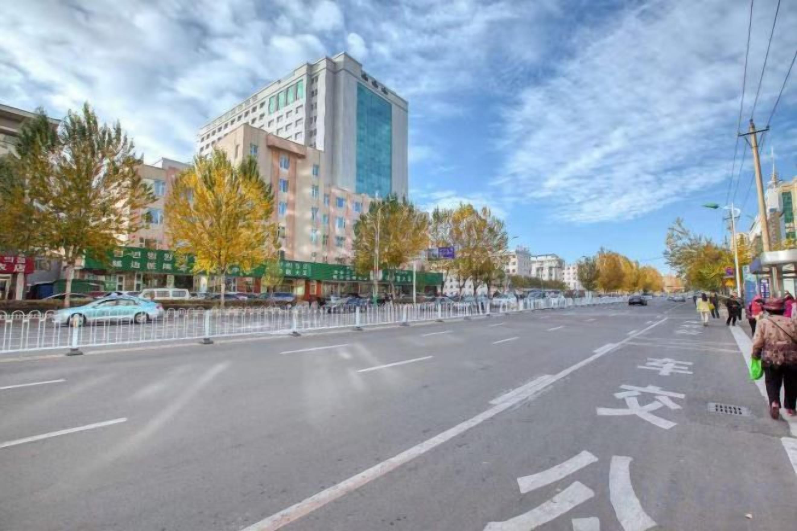 A multi-lane road with a pedestrian crossing, a tall building with reflective windows, and trees with autumn leaves.