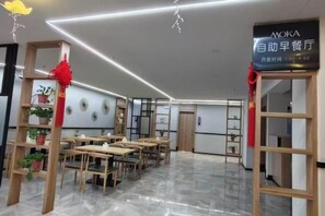 Ein Restaurantinneres mit Tischen und Stühlen, ein Schild, das ein Selbstbedienungsfrühstück anzeigt, und ein sauberes, modernes Design.